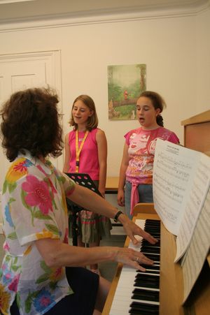 Frau am Klavier gibt zwei Mädchen Gesangsunterricht